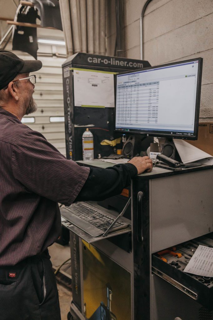 Technician using a computer at Lititz Collision to manage collision repair estimates and diagnostics, with tools and equipment visible in the background.