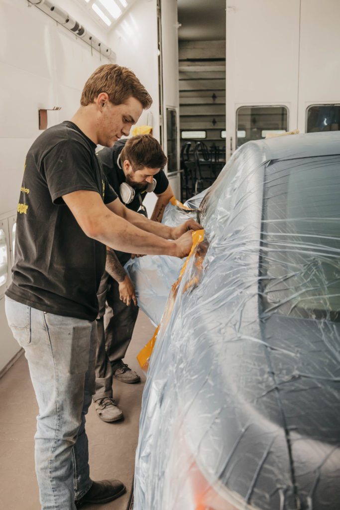 Two technicians applying protective film to a vehicle in an auto body repair shop, showcasing collision repair services.