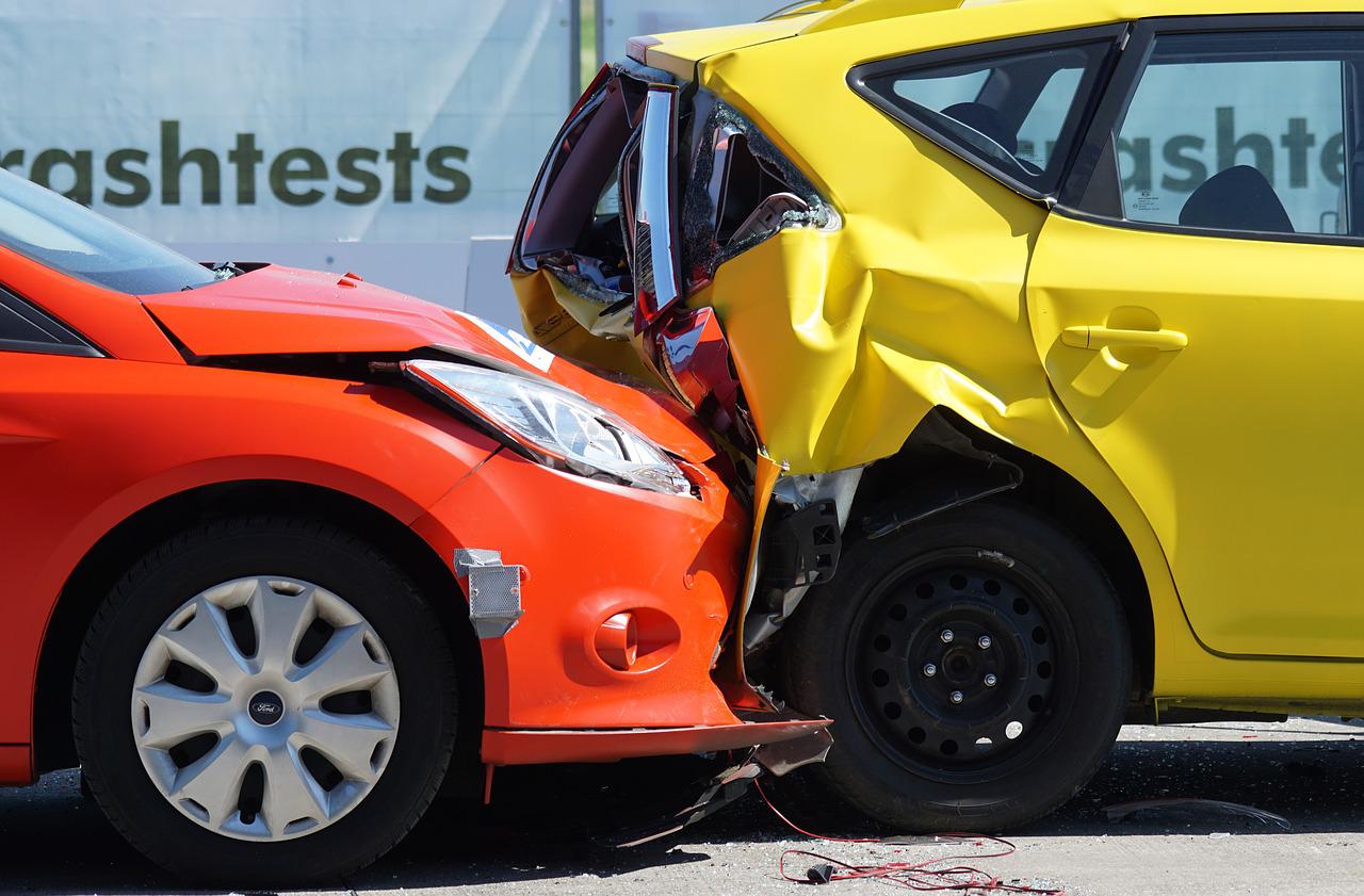 Red and yellow cars involved in a rear-end collision, showcasing significant damage, with a crash test backdrop emphasizing vehicle safety and accident prevention.