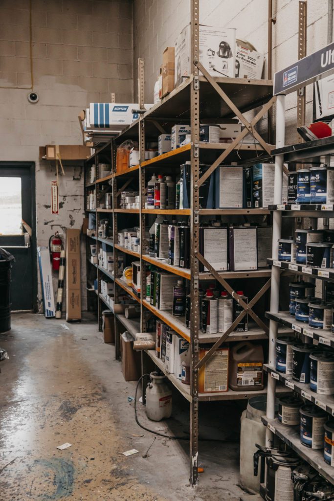 Shelves filled with various auto body repair supplies, including paint cans and chemicals, in a workshop setting at Lititz Collision, highlighting the tools used for collision repair services.