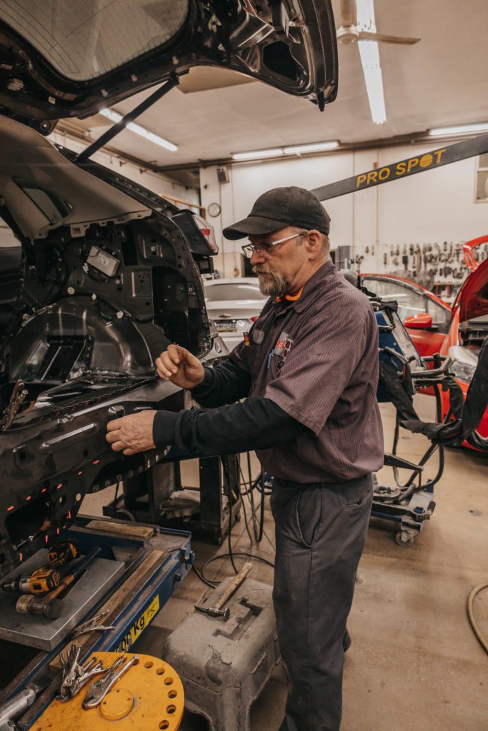 Auto body technician working on vehicle repair in a collision repair shop, showcasing tools and equipment used for structural restoration.