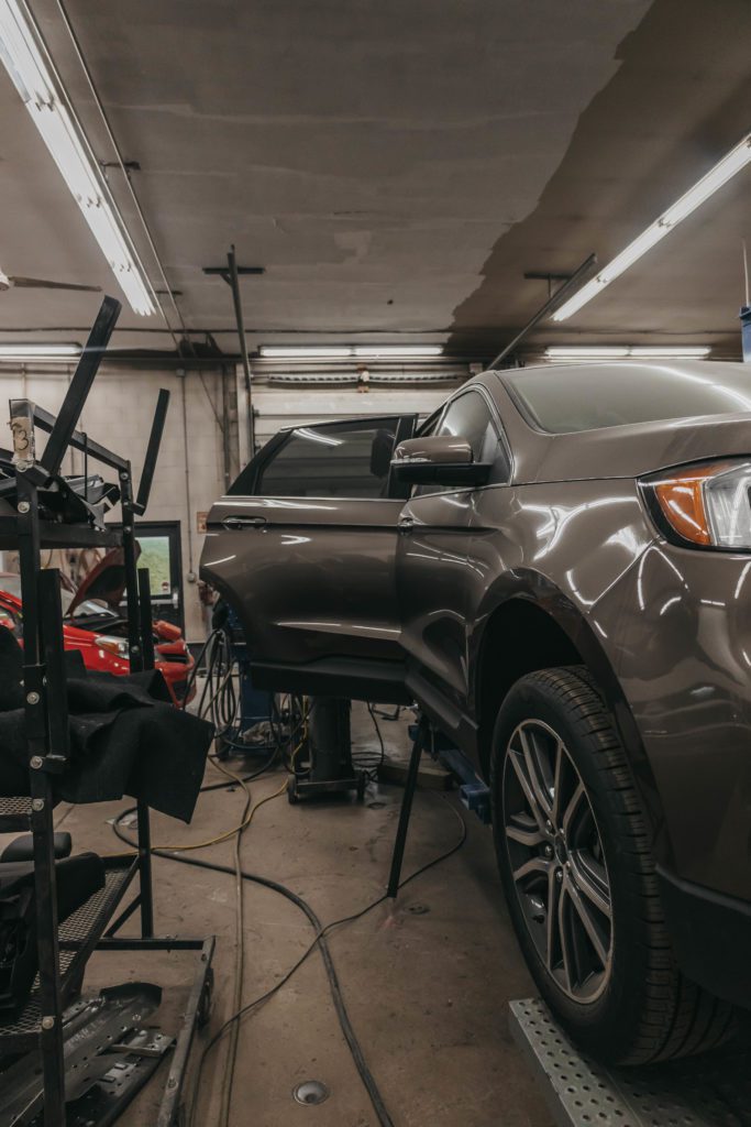 Auto body repair shop interior with a brown vehicle on a lift, showcasing tools and equipment for collision repair, emphasizing the restoration process at Lititz Collision.