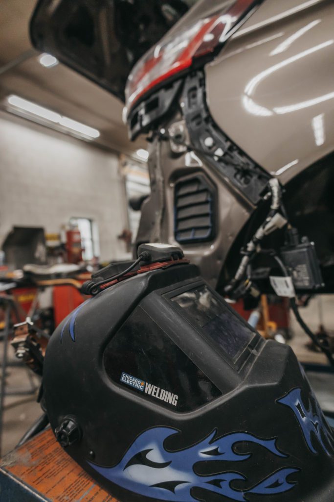 Welding helmet with flames design in an auto body shop setting, showcasing collision repair tools and equipment used for vehicle restoration.