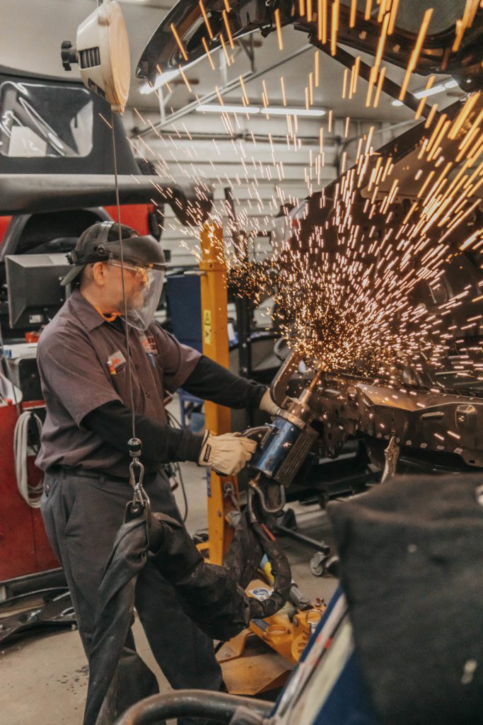 Technician performing collision repair work with a grinder, creating sparks, in an auto body shop setting, showcasing expertise in restoring vehicles at Lititz Collision.