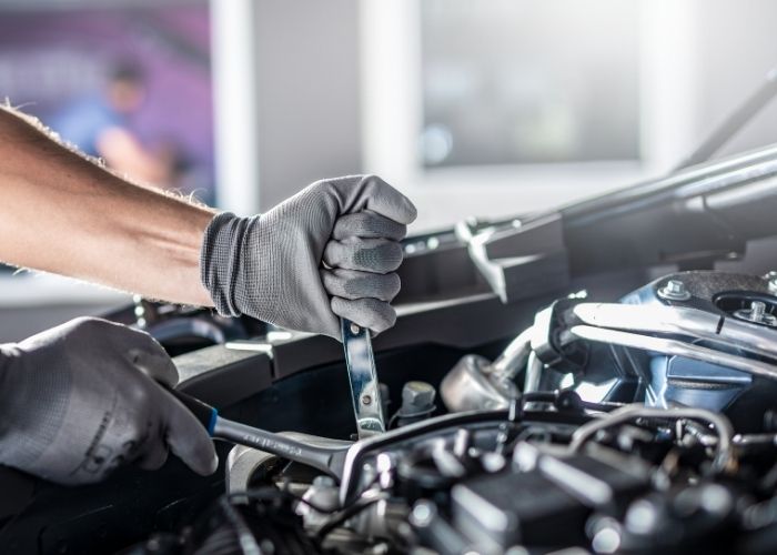Mechanic wearing gloves using a wrench on a car engine, showcasing quality vehicle repair services at Lititz Collision Myerstown.