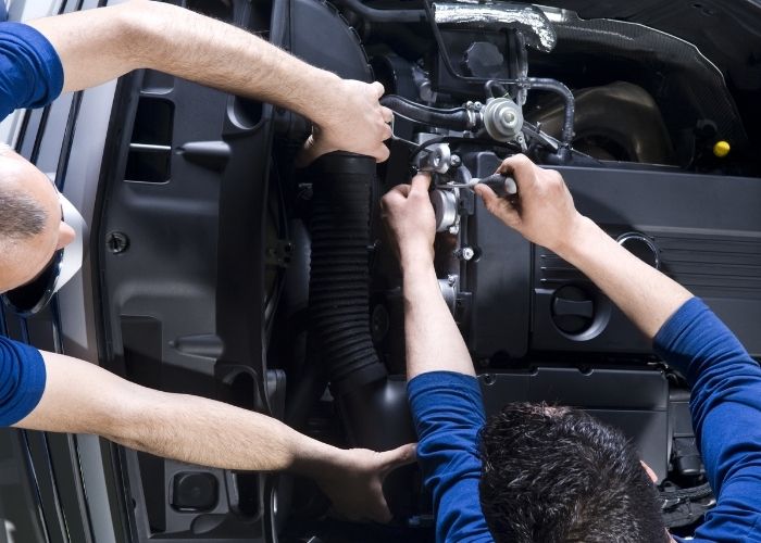 Two mechanics working on a car engine, adjusting components with tools, showcasing skilled craftsmanship in vehicle repair at Lititz Collision Lancaster.