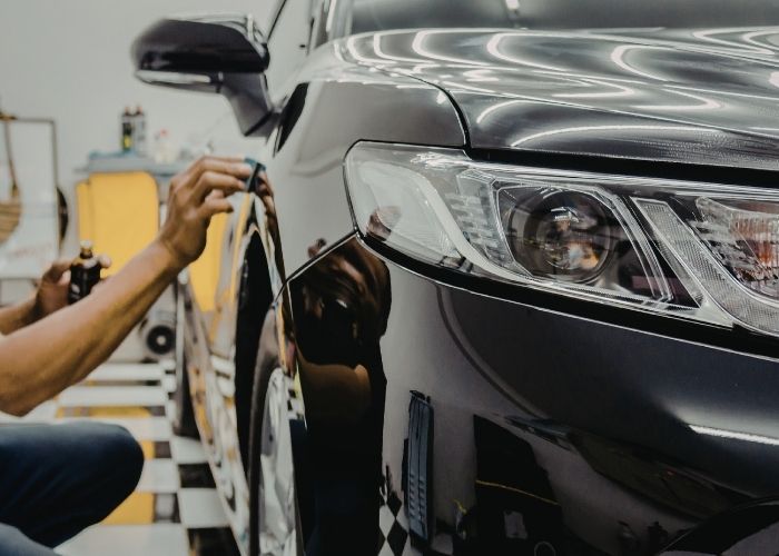 A person carefully polishes a reflective black car, highlighting the sleek front headlight.
