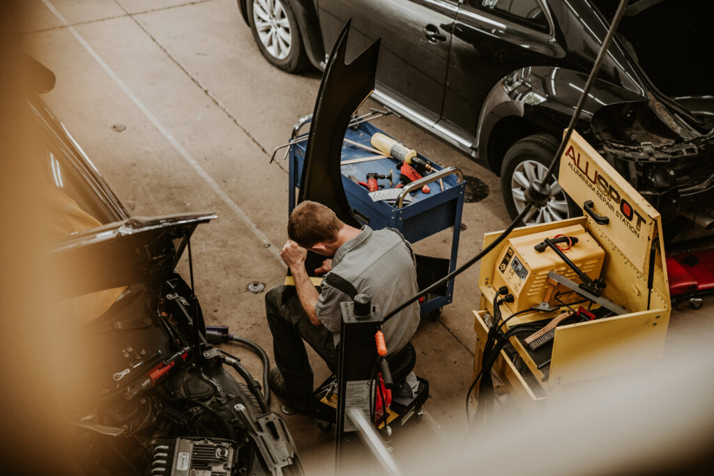 Mechanic working on vehicle repairs in an auto body shop, surrounded by tools and equipment, emphasizing collision repair services at Lititz Collision.