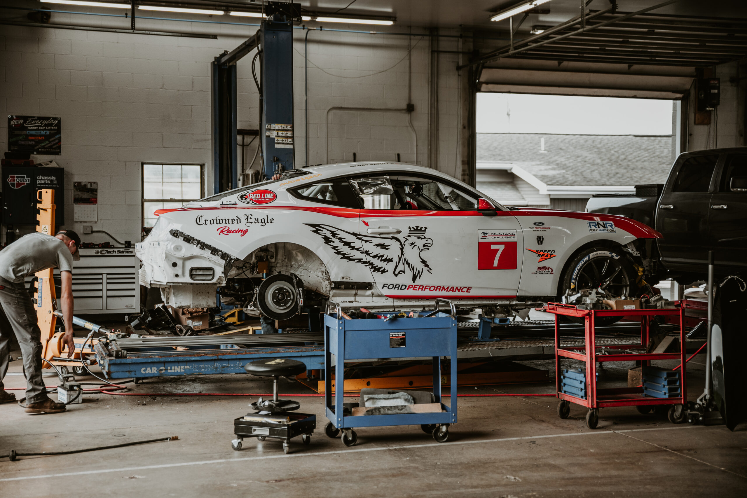 Race car being serviced in auto repair shop, showcasing mechanical and body repair capabilities, tools nearby, emphasizing comprehensive vehicle restoration.