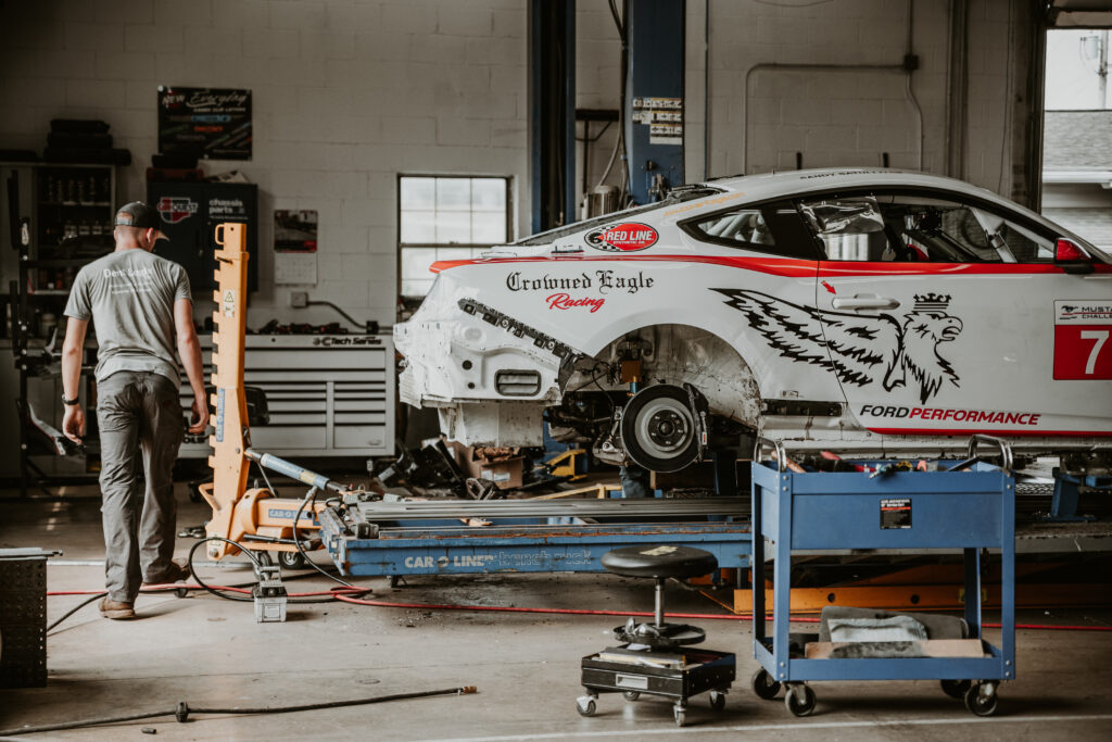 Mechanic working on a damaged racing car in an auto body repair shop, showcasing collision repair equipment and tools, highlighting the restoration process at Lititz Collision.