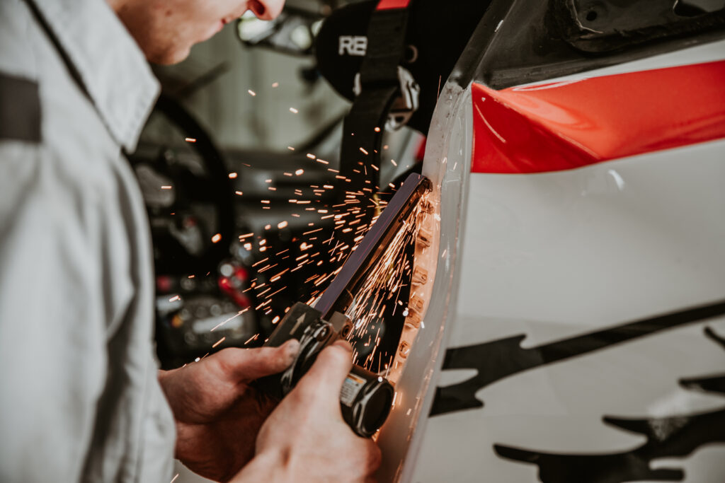 Technician performing collision repair on a vehicle, using a grinding tool that produces sparks, showcasing the restoration process at Lititz Collision auto body shop.