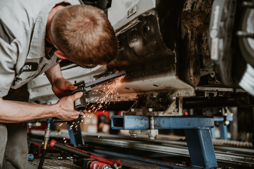 Auto body technician using a cutting tool on a vehicle's undercarriage, sparks flying, showcasing collision repair process at Lititz Collision.