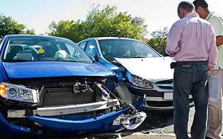 Two men inspecting damage on a blue car after a collision, with another vehicle in the background, highlighting post-accident assessment and repair needs.