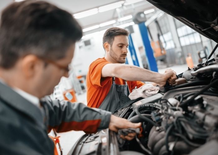 Two mechanics working on a car engine in a garage, focused on their tasks with tools and parts visible around them, representing quality automotive repair at Lititz Collision.
