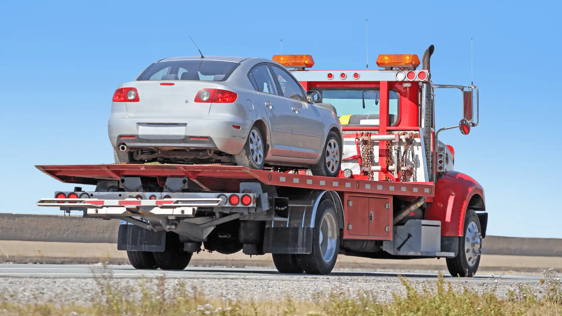 Silver sedan being towed on a red tow truck, illustrating emergency car towing services in Lancaster County after an accident.