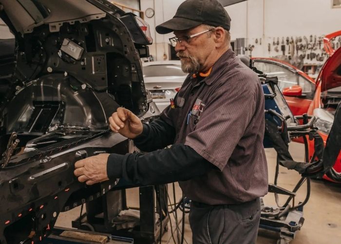 A man repairs a car in a garage, surrounded by tools and equipment, focused on his work.