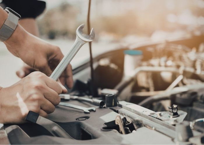Hands holding a wrench working on a car engine, illustrating mechanical repair services at Lititz Collision near Jonestown.